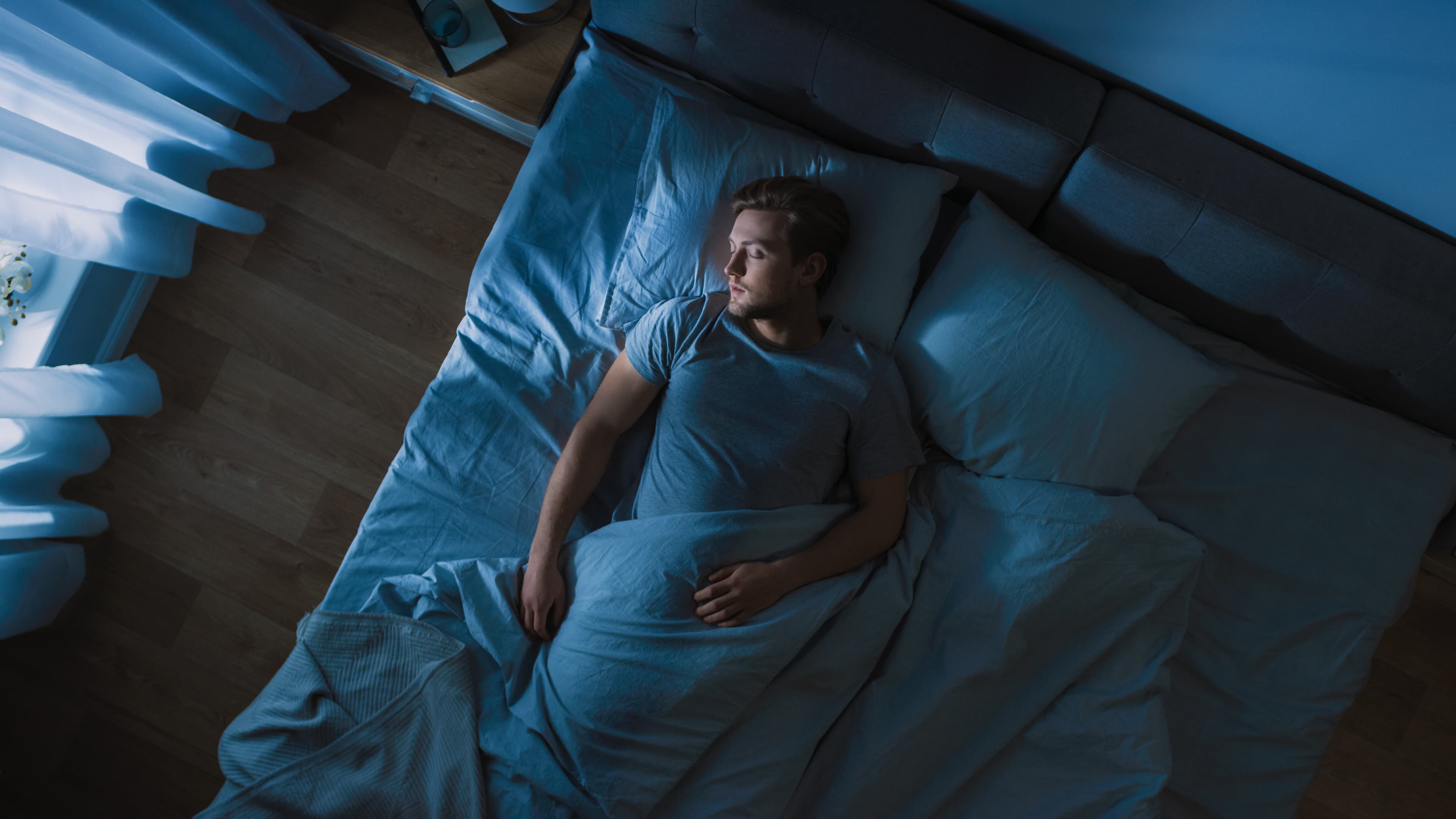 A man asleep in bed at night, seen from above, with the covers pulled up