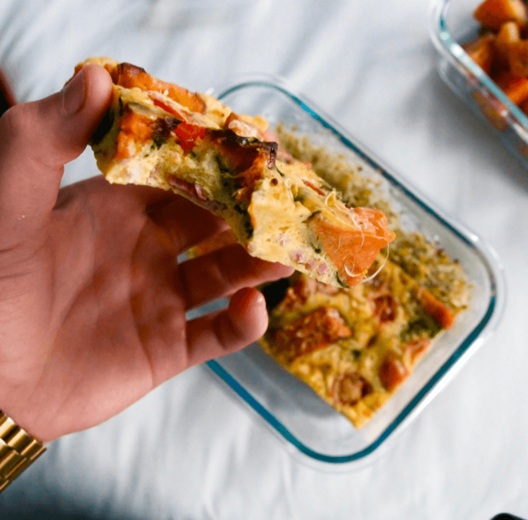 A slice of salmon and vegetable frittata lifted from a glass meal-prep container